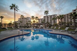Ein Pool in einem Resort mit Palmen, Liegestühlen und einem Sonnenuntergangshimmel.