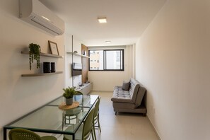 Un espacio habitable compacto con una mesa de comedor de cristal, un sofá gris y un ventanal que ofrece vistas al exterior.