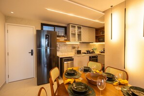 Una cocina moderna con horno integrado, un refrigerador y un comedor con una mesa preparada para dos.