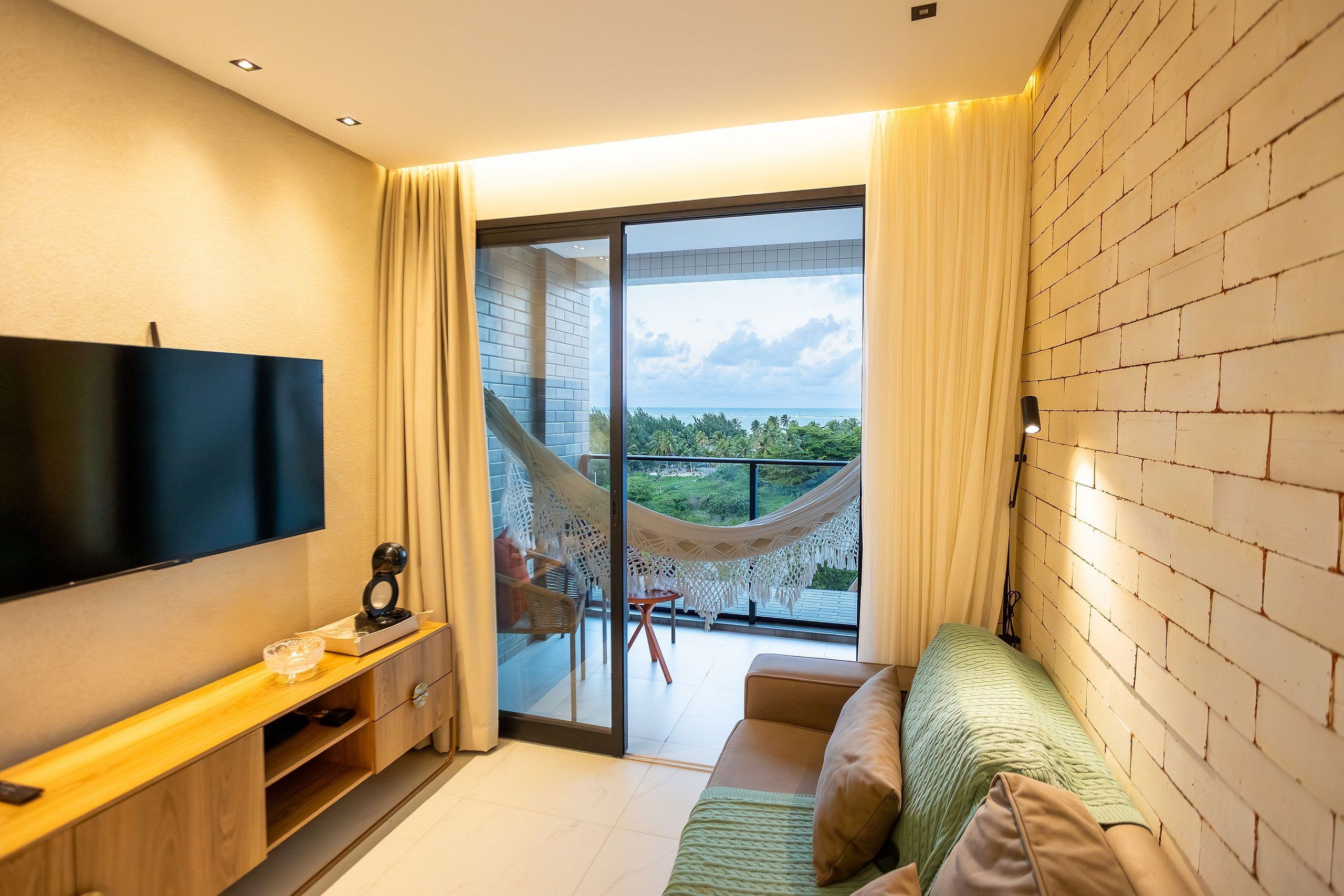 A modern living room with a flat-screen TV, a wooden console table, a sofa, and a balcony with a hammock.