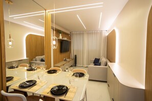 Un espace repas moderne avec une longue table dressée pour deux personnes, un canapé et un téléviseur fixé au mur.