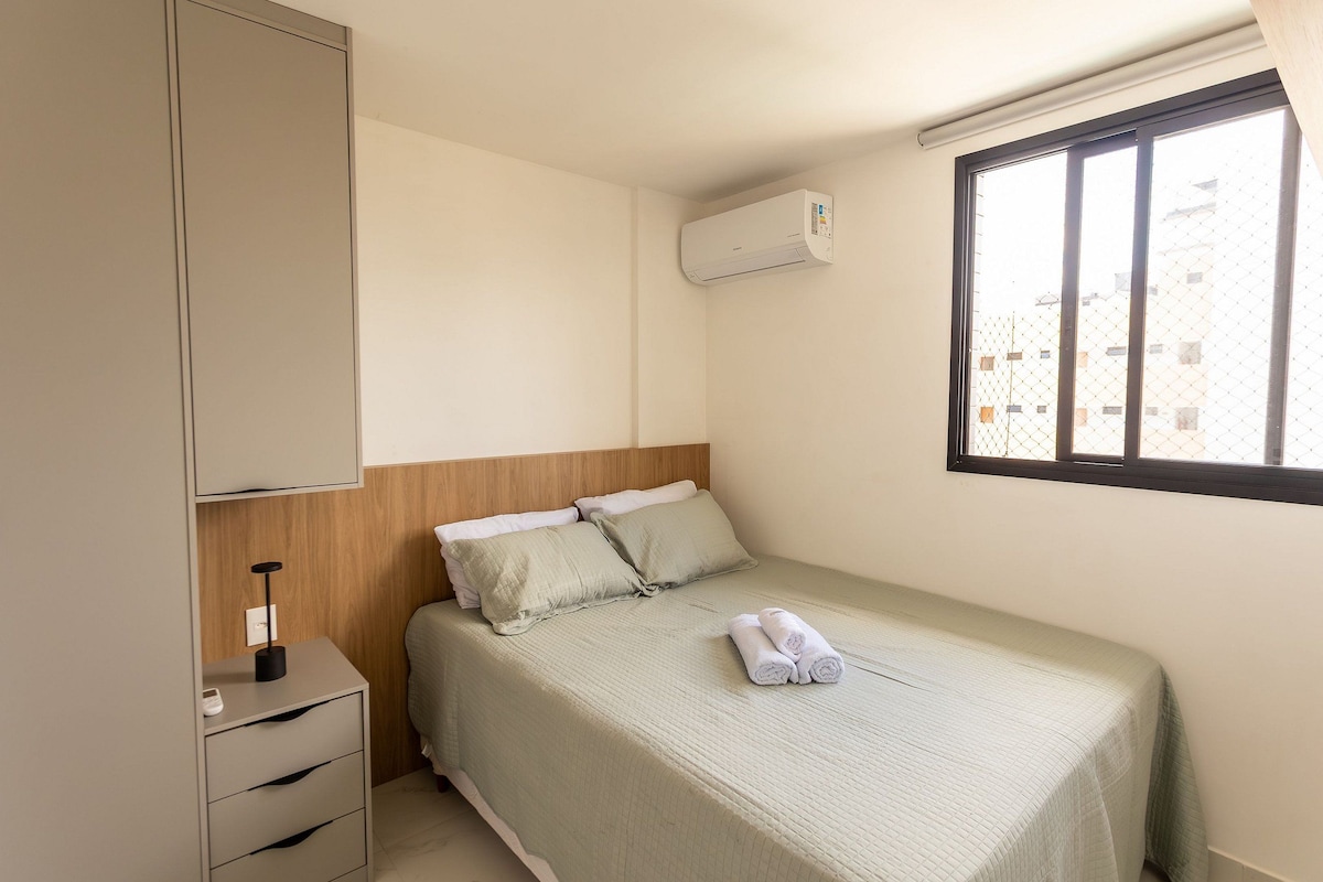 Ein Einzelbett mit grüner Bettdecke und zwei Kissen, ein Nachttisch mit Lampe, ein Kleiderschrank und eine Wandaircondition.