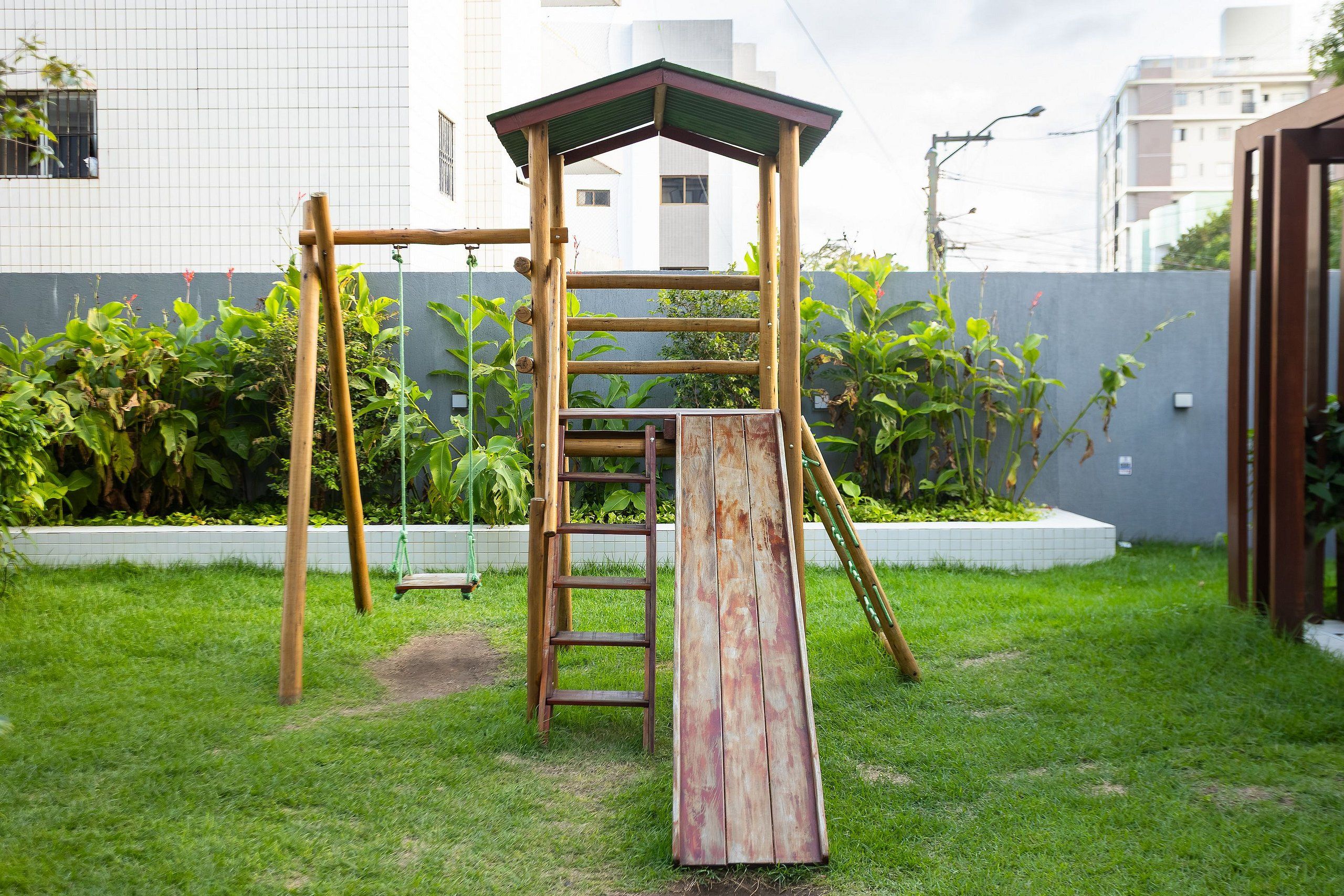 A wooden playground structure with a ladder and slide, surrounded by grass and plants.