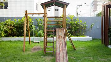 A wooden playground structure with a ladder and slide, surrounded by grass and plants.