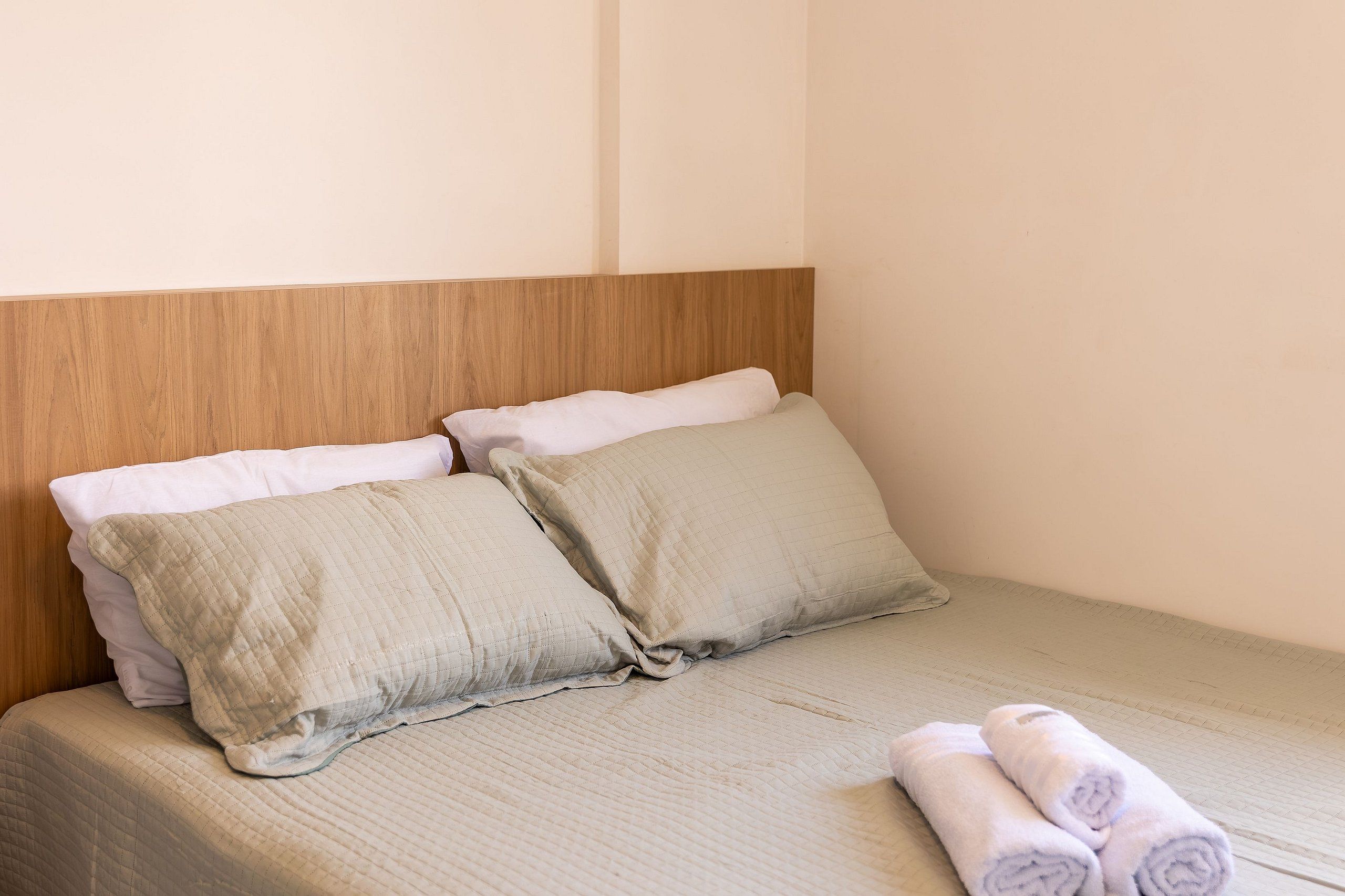 Una cama bien hecha con una colcha acolchada, dos almohadas y un par de toallas enrolladas.