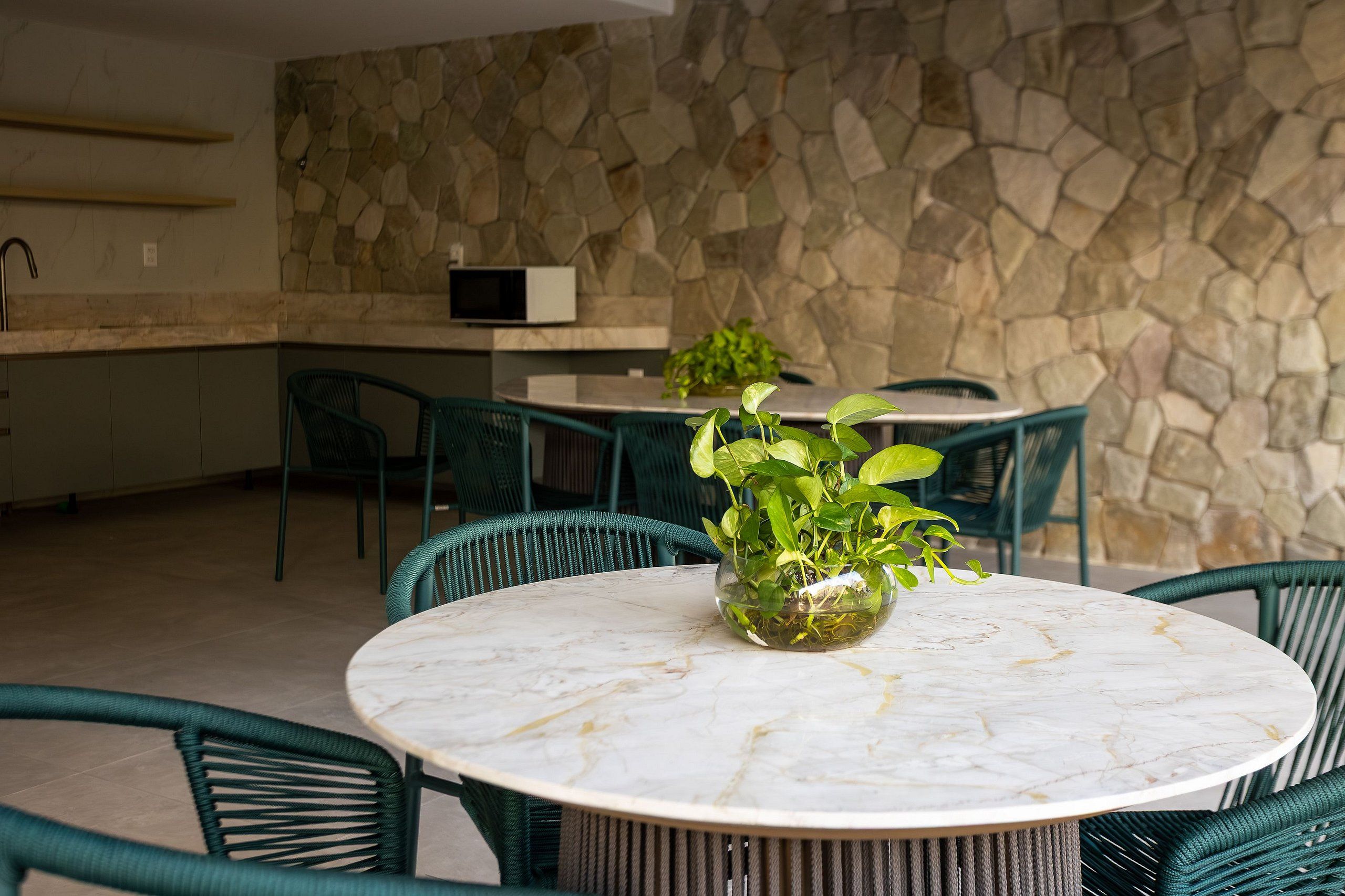 A round table with chairs, a potted plant, and a stone wall in the background.