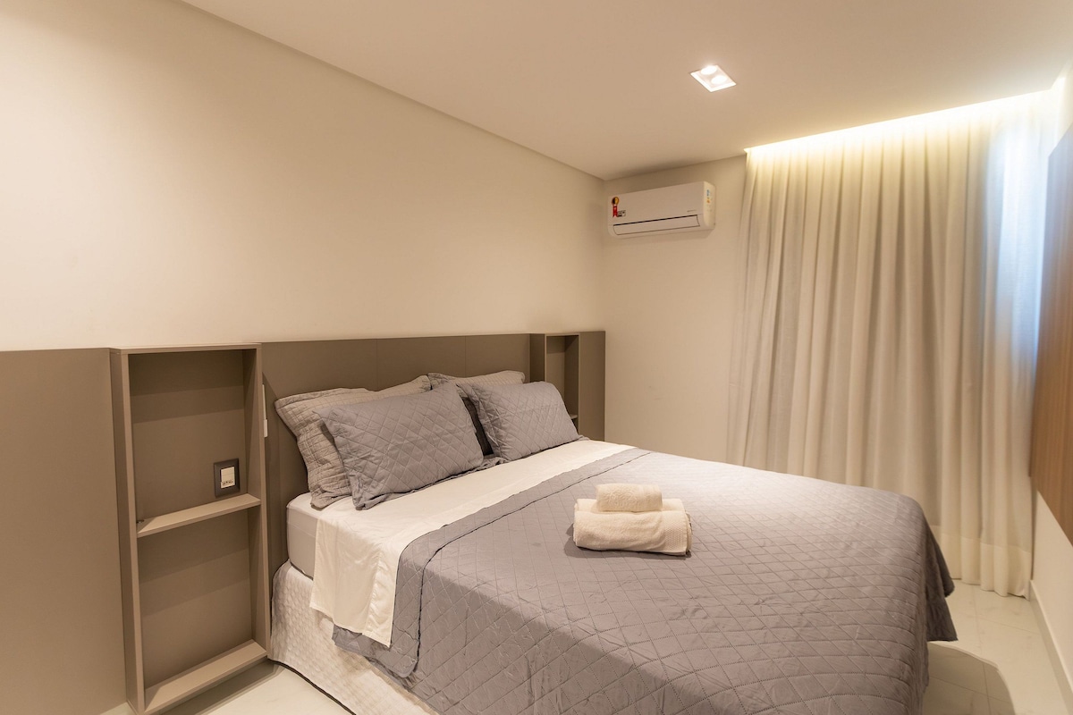 Ein Schlafzimmer mit einem Bett, einem Nachttisch, einer Wand-Klimaanlage und einem Fenster mit Vorhängen.