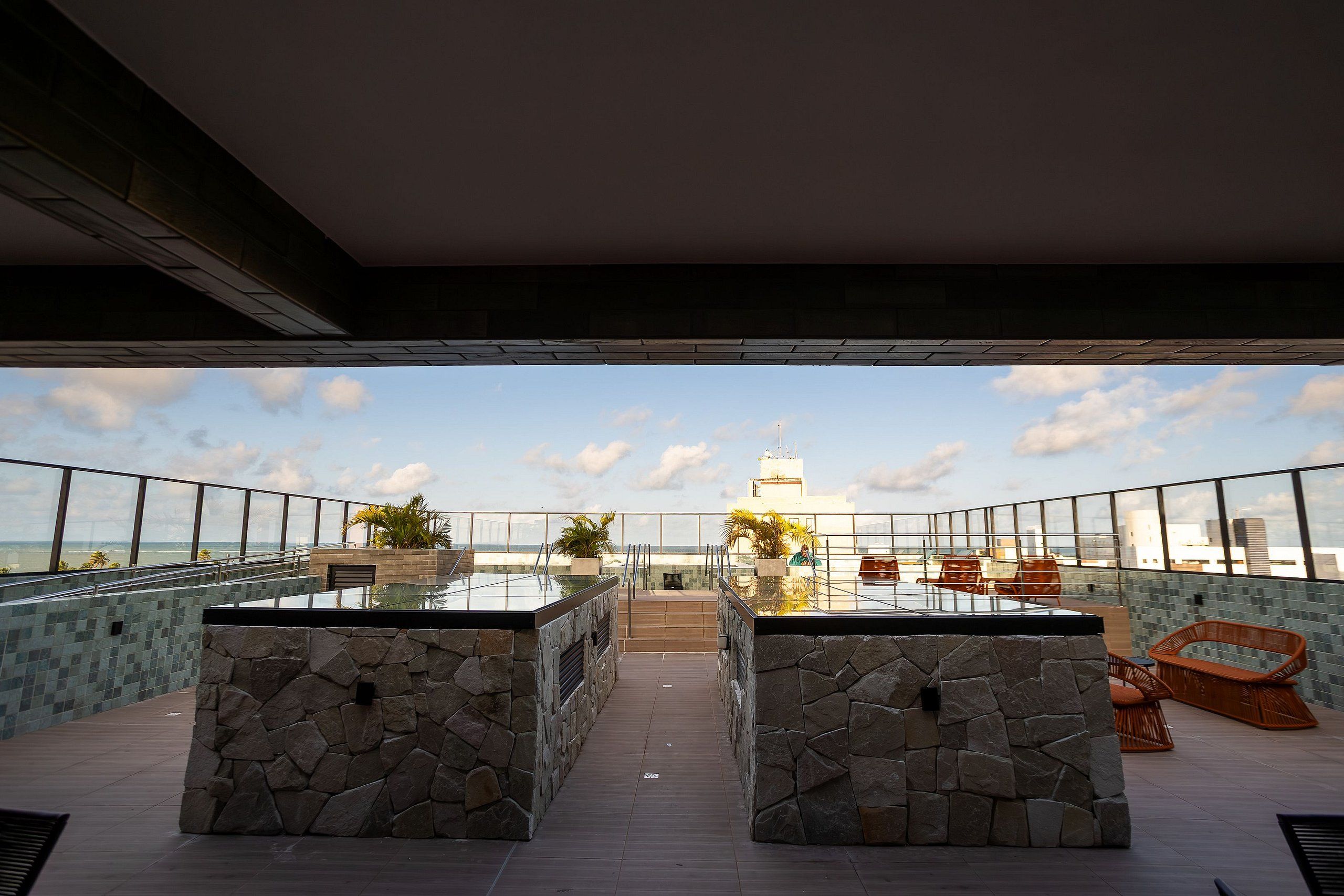 Um terraço no telhado com parede de pedra, mesa de vidro e cadeiras de vime.