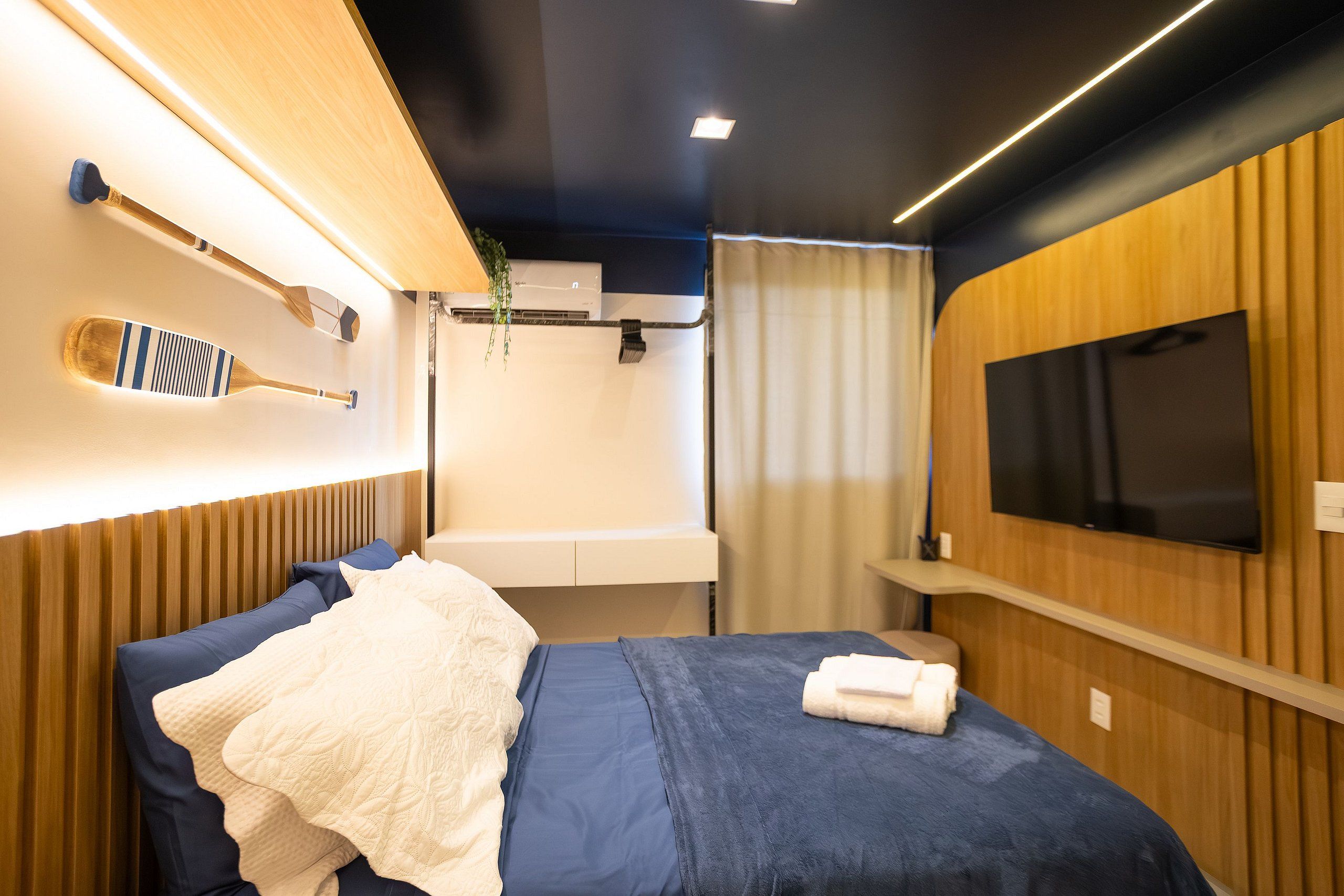 A modern bedroom with a bed, a mounted television, and a wall-mounted air conditioning unit.
