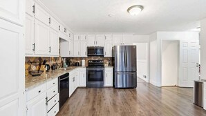A modern kitchen with white cabinets, stainless steel appliances, and a wooden floor.