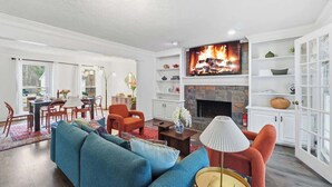 A living room with a fireplace, a television, and a dining area with chairs and a table.
