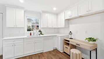 Una cocina moderna con armarios blancos, encimera de madera y un escritorio empotrado con una planta.