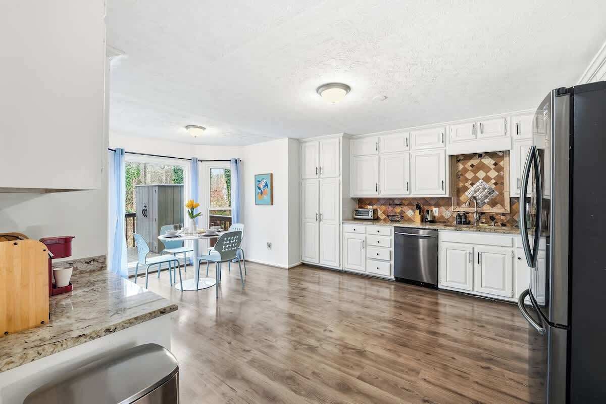 A kitchen with white cabinets, a black refrigerator, and a dining area with a table and chairs.