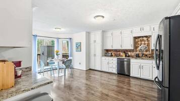 A kitchen with white cabinets, a black refrigerator, and a dining area with a table and chairs.