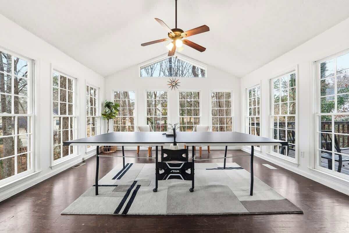 Une pièce spacieuse avec une grande table, un ventilateur de plafond et de grandes fenêtres donnant sur l’extérieur.