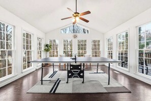 Una habitación amplia con una mesa grande, un ventilador de techo y ventanas que ofrecen vistas al exterior.