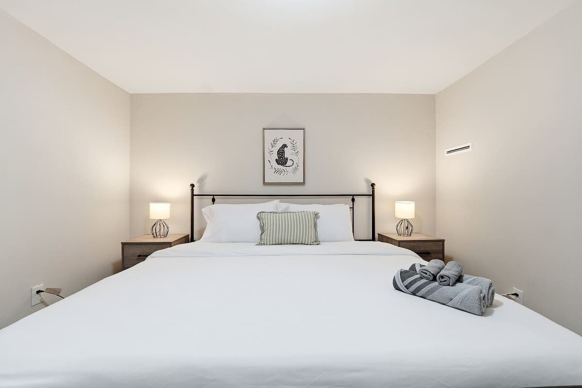A hotel room with a large bed, two bedside lamps, a framed artwork on the wall, and a neatly made bed with towels.