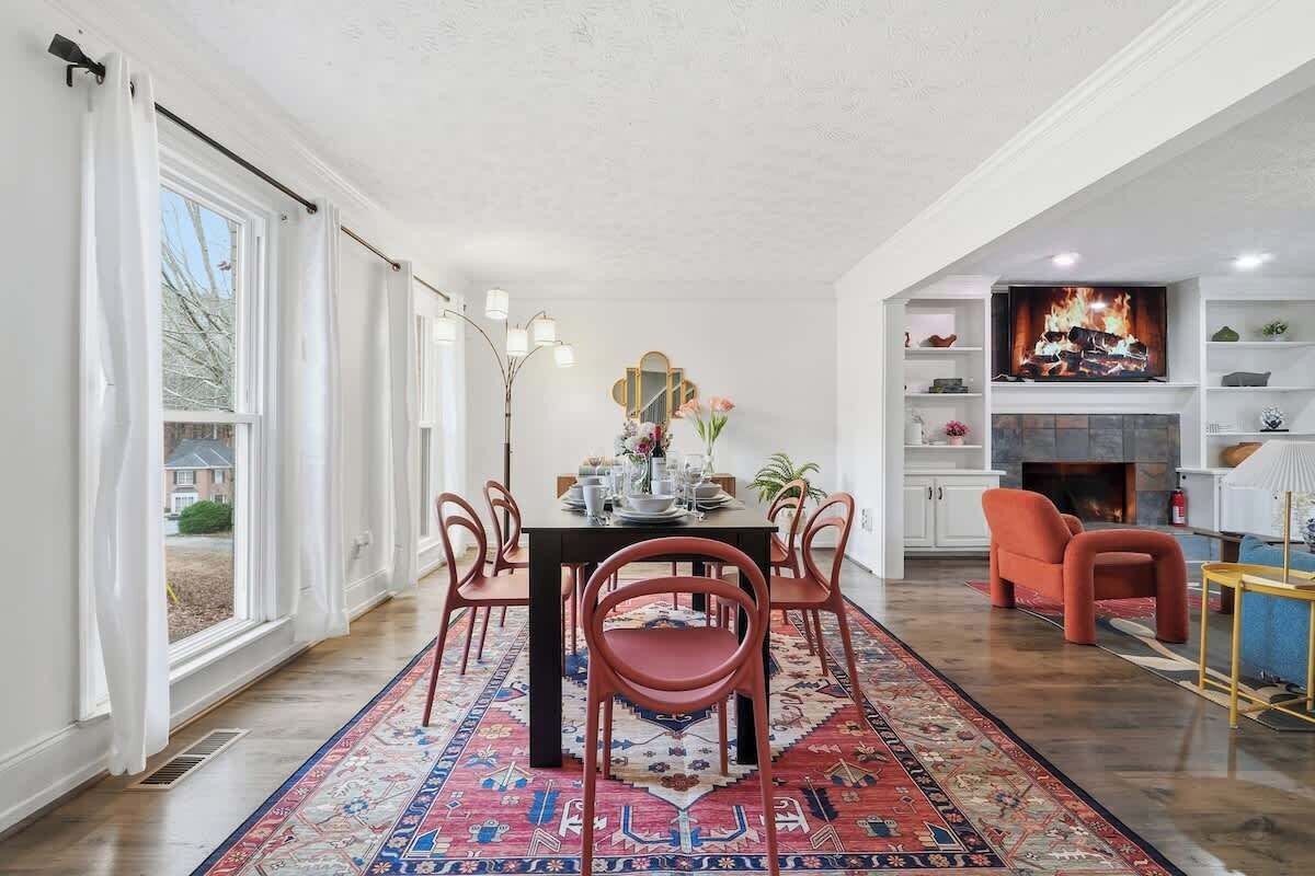 A dining area with a table set for four, surrounded by chairs, a patterned rug, and a fireplace with a mantel display.