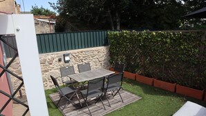 En terrasse med et bord og stole, en stenvæg og en grøn hæk.