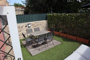A patio with a table and chairs, a stone wall, and a green hedge. - Montebelo I (Porto)