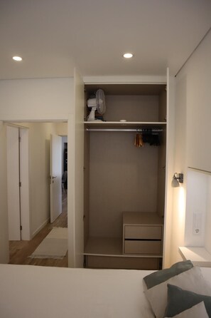 Ein Schlafzimmer mit Bett, Nachttisch, Kleiderschrank mit Kleidung und einem kleinen Schreibtisch mit Stuhl.