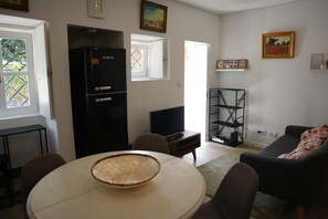 A living room with a TV, a black refrigerator, a dining table with chairs, a sofa, and a bookshelf. - Montebelo I (Porto)