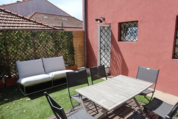 Eine Terrasse mit einem Holztisch und -stühlen, einem weißen Sofa und einem Gitterzaun.