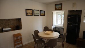 Et spiseområde med et rundt bord, stole, en skål, et køleskab og kunst på væggen.