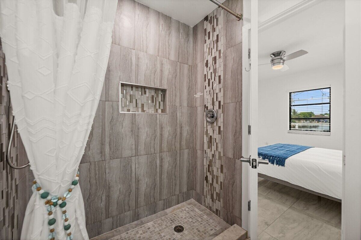 Um chuveiro com parede de azulejos estampados, cortina de chuveiro branca e um chuveiro visível.