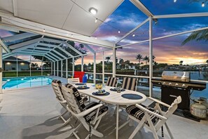 Ein Essbereich im Freien mit Pool, Grill und Blick auf den Sonnenuntergang.