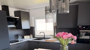 Una cocina moderna con una isla central, armarios negros, un lavamanos de acero inoxidable y una lámpara colgante.