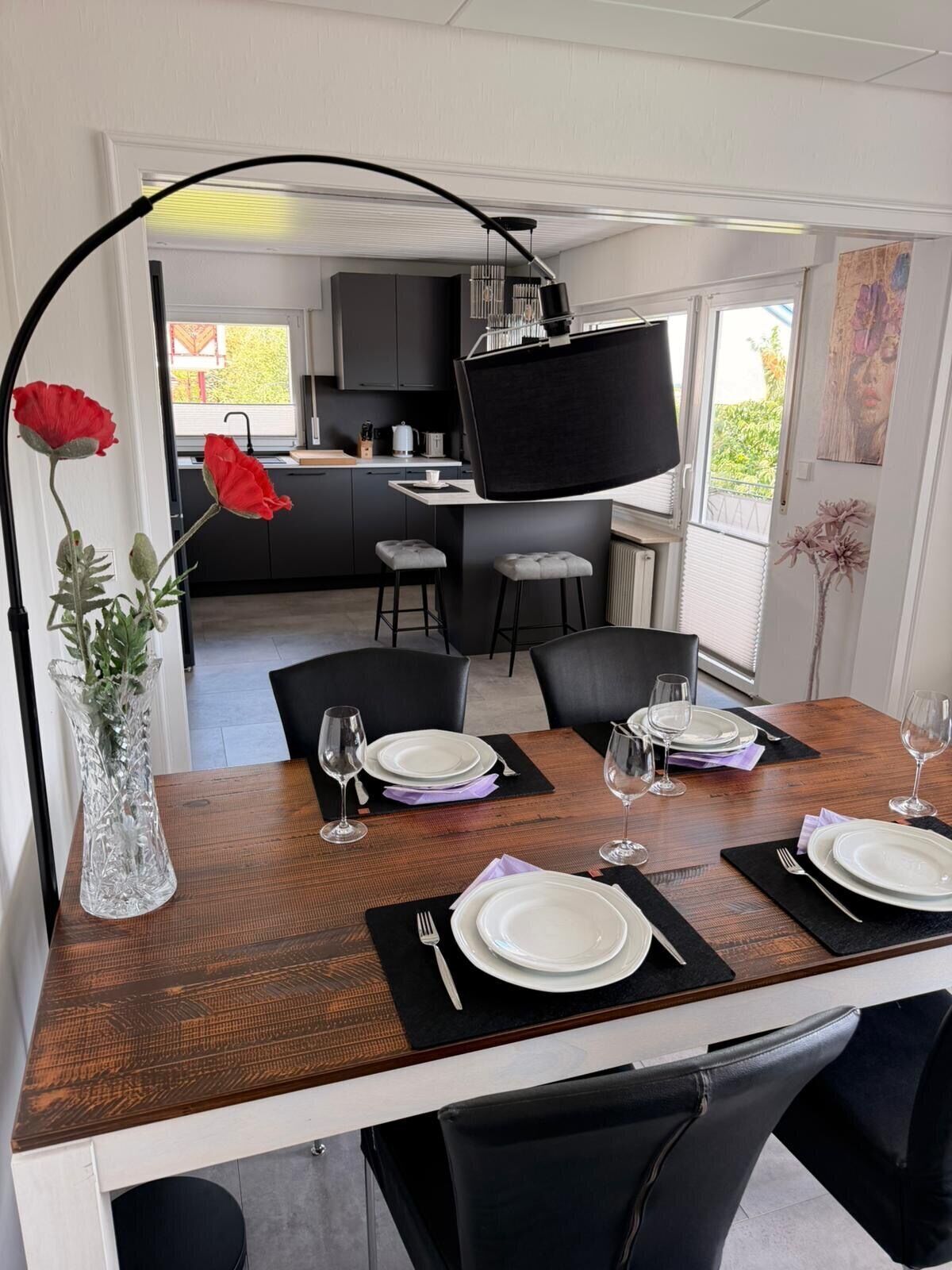 A dining area with a wooden table set for four, black chairs, and a large black floor lamp.