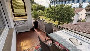Un balcón con una mesa y sillas, un tapete estampado y vistas a un jardín y casas.