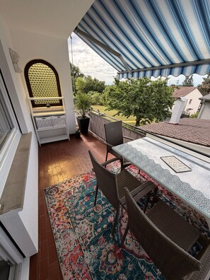 A balcony with a table and chairs, a patterned rug, and a view of a garden and houses. - Modernly furnished & fully renovated Holiday apartment (Owingen)