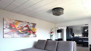 Una sala de estar moderna con un sofá seccional gris, un cuadro abstracto grande y un comedor con una lámpara negra.