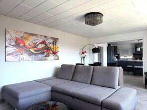 A modern living room with a gray sectional sofa, a large abstract painting, and a dining area with a black lamp. - Modernly furnished & fully renovated Holiday apartment (Owingen)