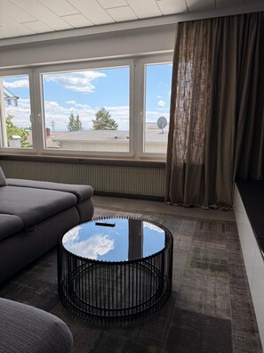 A room with a sofa, a round table with a glass top, and a view of the outside through large windows. - Modernly furnished & fully renovated Holiday apartment (Owingen)
