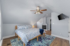 Um quarto com cama, ventilador de teto, lareira e televisão fixada na parede.