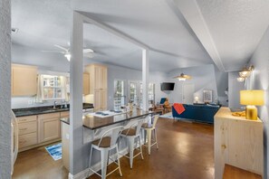 Une cuisine spacieuse avec un grand îlot central, des tabourets de bar et un coin repas agrémenté d’un canapé bleu.
