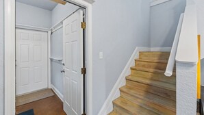 Un couloir avec un escalier en bois, une porte blanche et un mur blanc.
