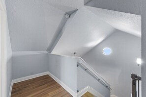 Um canto de um quarto com chão de madeira, parede branca e teto com iluminação embutida.