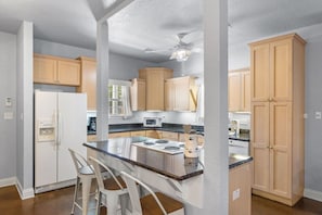 A modern kitchen with a central island, wooden cabinets, and a built-in microwave. - 3BR Coastal Retreat | 10 Min to Beaches (Pensacola)