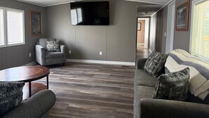 A living room with a gray sofa, a gray armchair, a wooden coffee table, and a flat-screen TV mounted on the wall. - Peaceful 3-Bedroom home on Lake Oahe (Pierre)