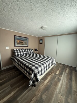A bedroom with a bed, a framed picture on the wall, a lamp, and a wardrobe. - Peaceful 3-Bedroom home on Lake Oahe (Pierre)