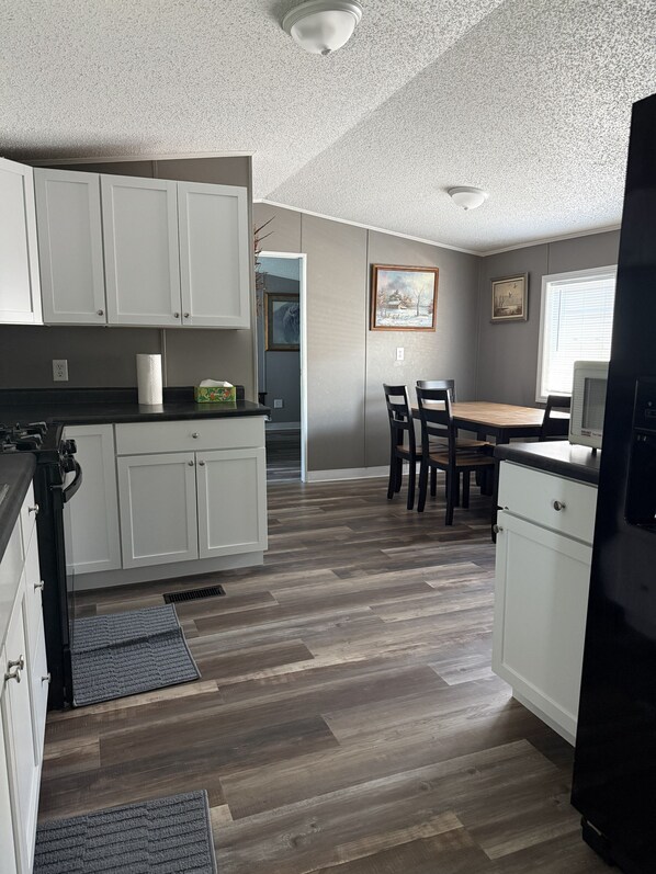A kitchen with white cabinets, a dining table with chairs, and a refrigerator. - Peaceful 3-Bedroom home on Lake Oahe (Pierre)