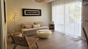 A living room with a sofa, a round coffee table, a wicker chair, a floor lamp, and a framed artwork on the wall. - Azure Treasure Chest (La Londe-les-Maures)