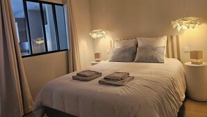 A neatly made bed with pillows, a bedside lamp, and a window with curtains. - Azure Treasure Chest (La Londe-les-Maures)
