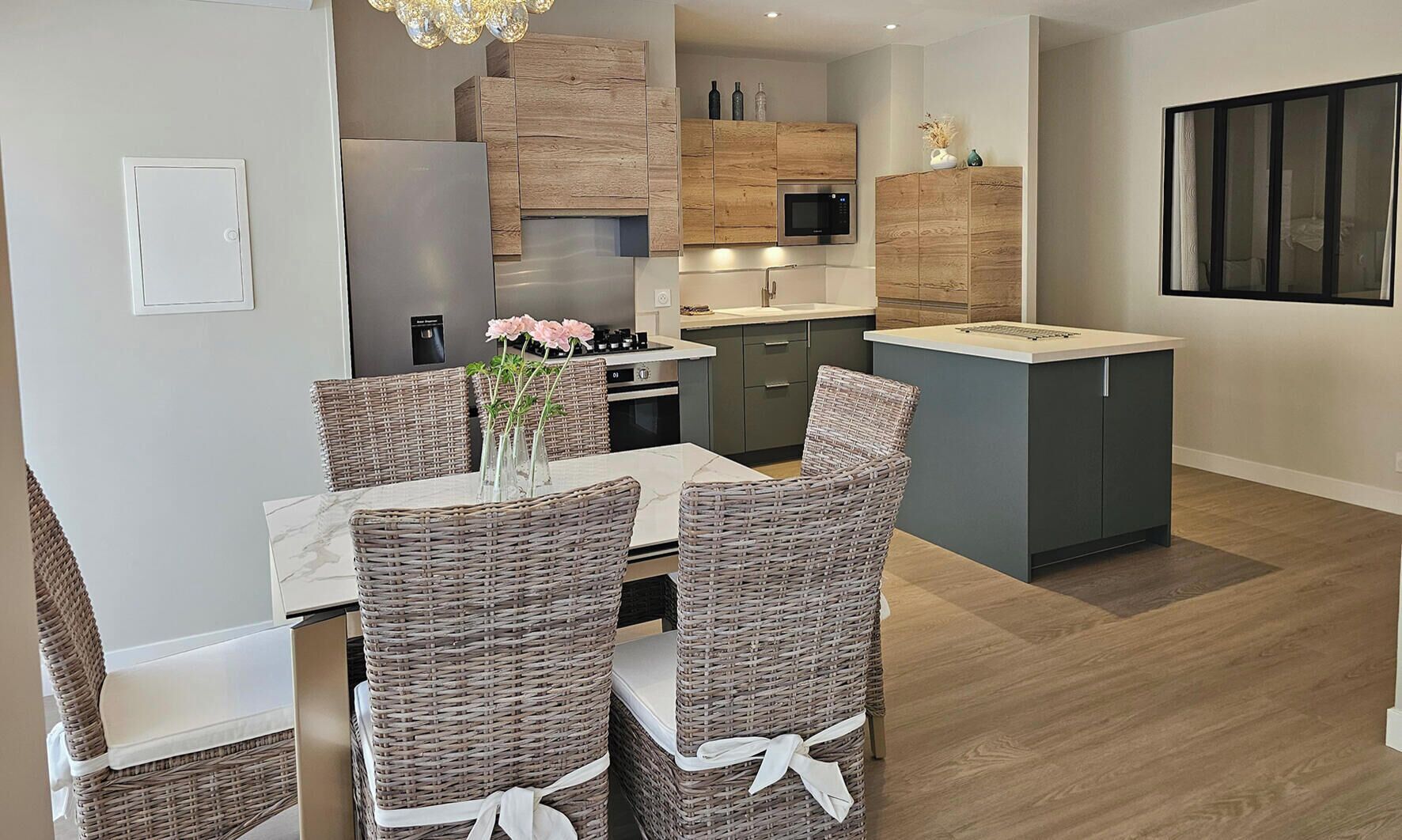 Eine moderne Küche mit Holzausstattung, einer eingebauten Mikrowelle und einem Essbereich mit Korbstühlen und einem Marmortisch.