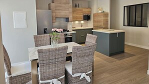 A modern kitchen with wooden cabinets, a built-in microwave, and a dining area with wicker chairs and a marble table. - Azure Treasure Chest (La Londe-les-Maures)