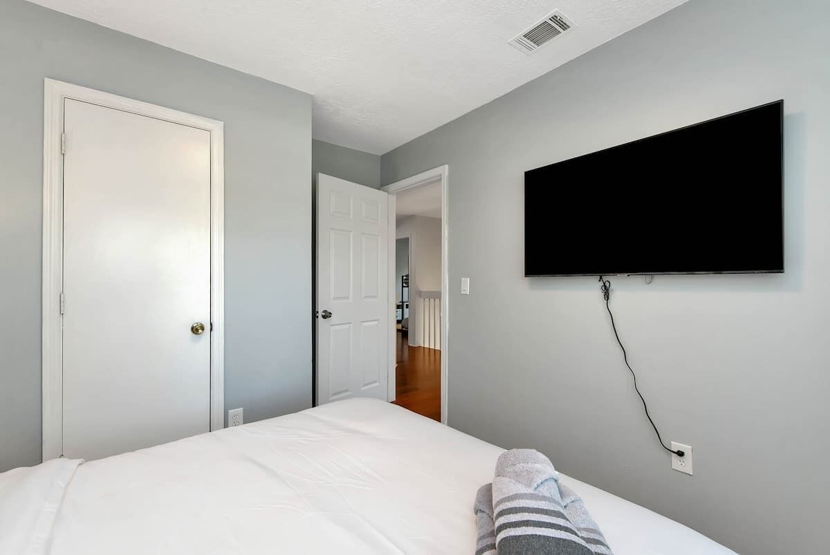 Un dormitorio con una cama, un televisor montado en la pared y una puerta que da a otra habitación.